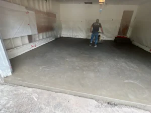 NG Masonry technician running a ride on power trowel across a freshly poured garage floor with plastic wall protection, serving Chili NY