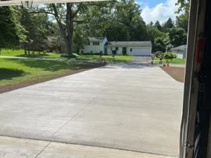 Wide broom finished concrete driveway viewed from inside an open garage looking out toward a residential street, by NG Masonry serving East Rochester NY