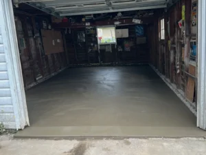 Empty wood plank walled garage with vintage signs on the back wall and a freshly poured smooth gray concrete floor, by NG Masonry serving Fairport NY