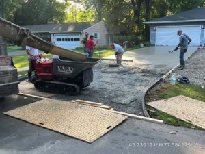 NG Masonry crew placing fresh concrete from a tracked buggy onto a rebar prepped driveway pad beside a pink ranch home, serving Farmington NY