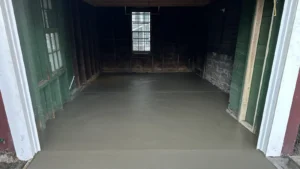 Wood framed garage interior with green sided walls and a freshly poured smooth gray concrete floor under a multi pane window, by NG Masonry serving Gates NY