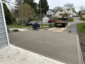 NG Masonry workers finishing a freshly poured broom textured concrete driveway extension from an open garage door, serving Geneva NY