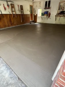 Garage interior with wood paneled lower walls and tools hanging on the back wall over a freshly poured smooth gray concrete floor, by NG Masonry serving Greece NY