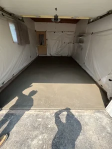 Garage interior taped off with plastic wall protection and a freshly poured smooth gray concrete floor curing, by NG Masonry serving Hilton NY