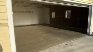 Open garage with exposed rafters and dark wood paneled back wall over a freshly poured smooth gray concrete floor, by NG Masonry serving Irondequoit NY
