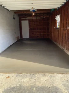 Empty garage interior with a wood paneled back wall, side door, and a freshly poured smooth gray concrete floor, by NG Masonry serving Mendon NY