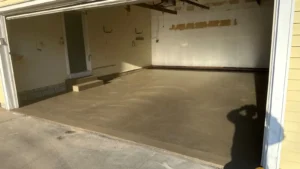 Open garage with side entry steps and a freshly poured smooth gray concrete floor curing in afternoon light, by NG Masonry serving Newark NY