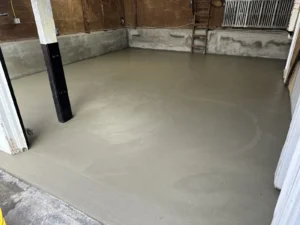 Old garage interior with brick walls, dark wood paneling, and a freshly poured smooth gray concrete floor catching daylight, by NG Masonry serving Rochester NY