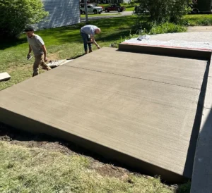 NG Masonry crew finishing edges on a freshly poured broom finished concrete shed pad in a residential yard, serving Rochester NY
