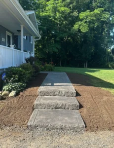Three tier stamped concrete step blocks with rock faced edges leading to a covered porch at a gray sided home, by NG Masonry serving Brockport NY