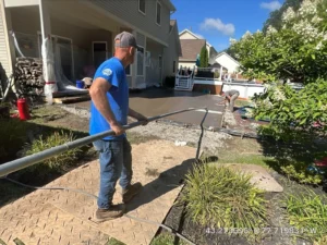 NG Masonry worker using a vibratory screed during a fresh stamped concrete patio pour beside a tan sided home, serving Canandaigua NY