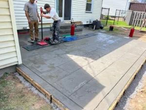 Two NG Masonry crew members stamping fresh wet concrete with ashlar slate texture at a white sided home, serving Chili NY