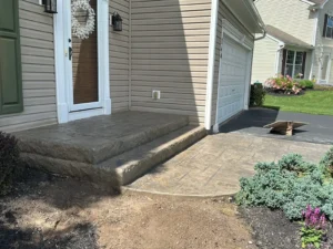Stamped concrete front step and matching driveway apron leading to the garage at a cream sided home, by NG Masonry serving East Rochester NY