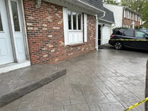 Wide ashlar slate stamped concrete driveway at a red brick home with white shutters, by NG Masonry serving Greece NY