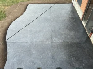 Large charcoal slate textured stamped concrete patio with curved edge along a sided home, by NG Masonry serving Henrietta NY