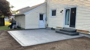 Light gray slate textured stamped concrete back patio with rock faced edge at a cream sided home, by NG Masonry serving Webster NY