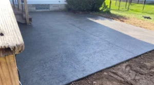 Charcoal slate textured stamped concrete walkway past a wooden post and chain link fence, by NG Masonry serving Williamson NY