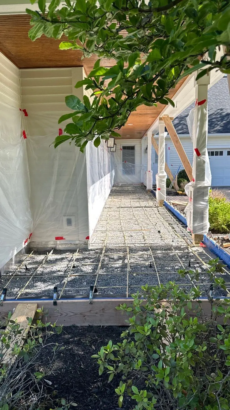 Wood form boards and rebar grid over a compacted gravel base for a covered front porch slab with plastic sheeting protection, by NG Masonry serving Fairport NY