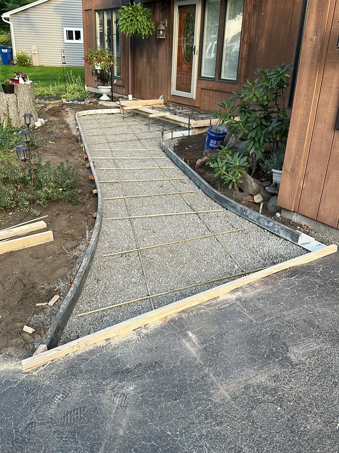 Wood form boards and rebar grid over compacted gravel for a new concrete walkway leading to the front door of a dark stained wood sided home, by NG Masonry serving Rochester NY