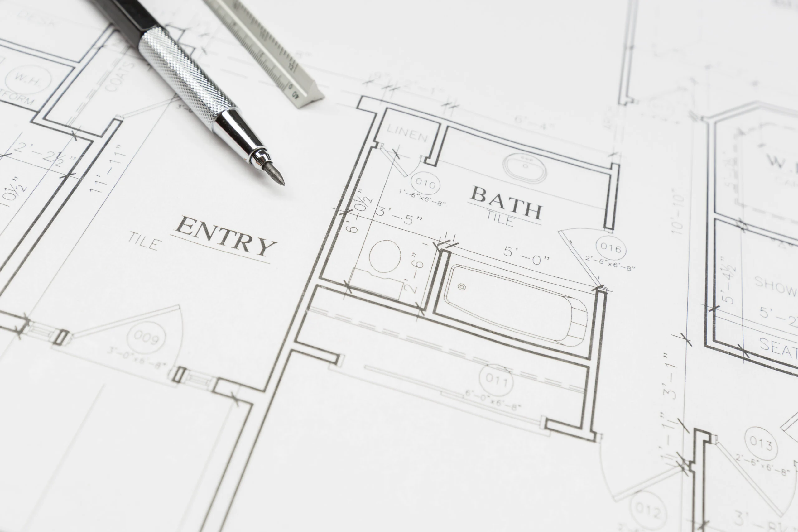Closeup of a hand drafted floor plan blueprint for a home addition showing entry and bathroom layouts with a drafting pen and rule on top, by NG Masonry serving Rochester NY