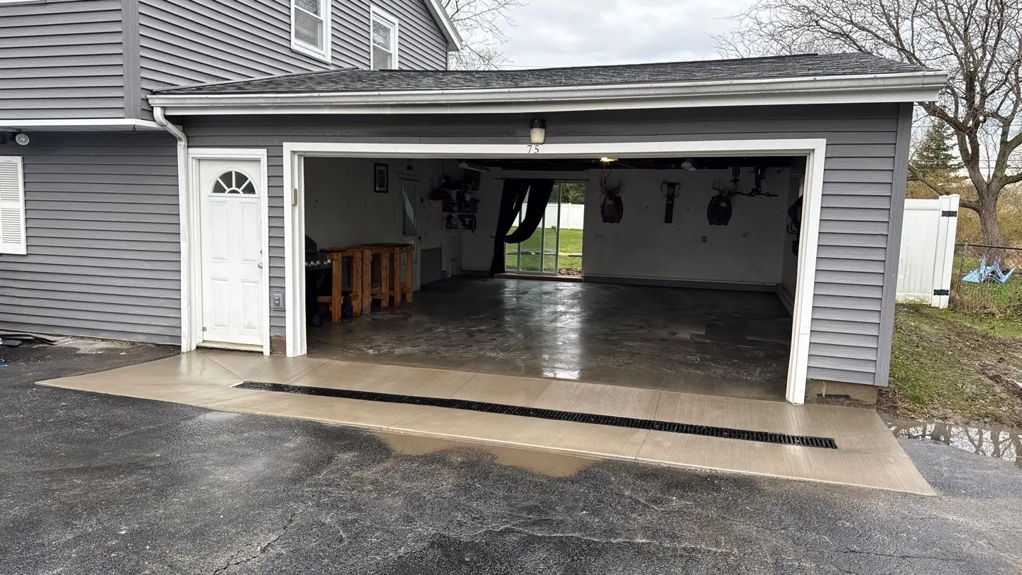 The finished concrete garage floor and new apron in Greece NY seen from the driveway, with the new trench drain sitting flush across the opening