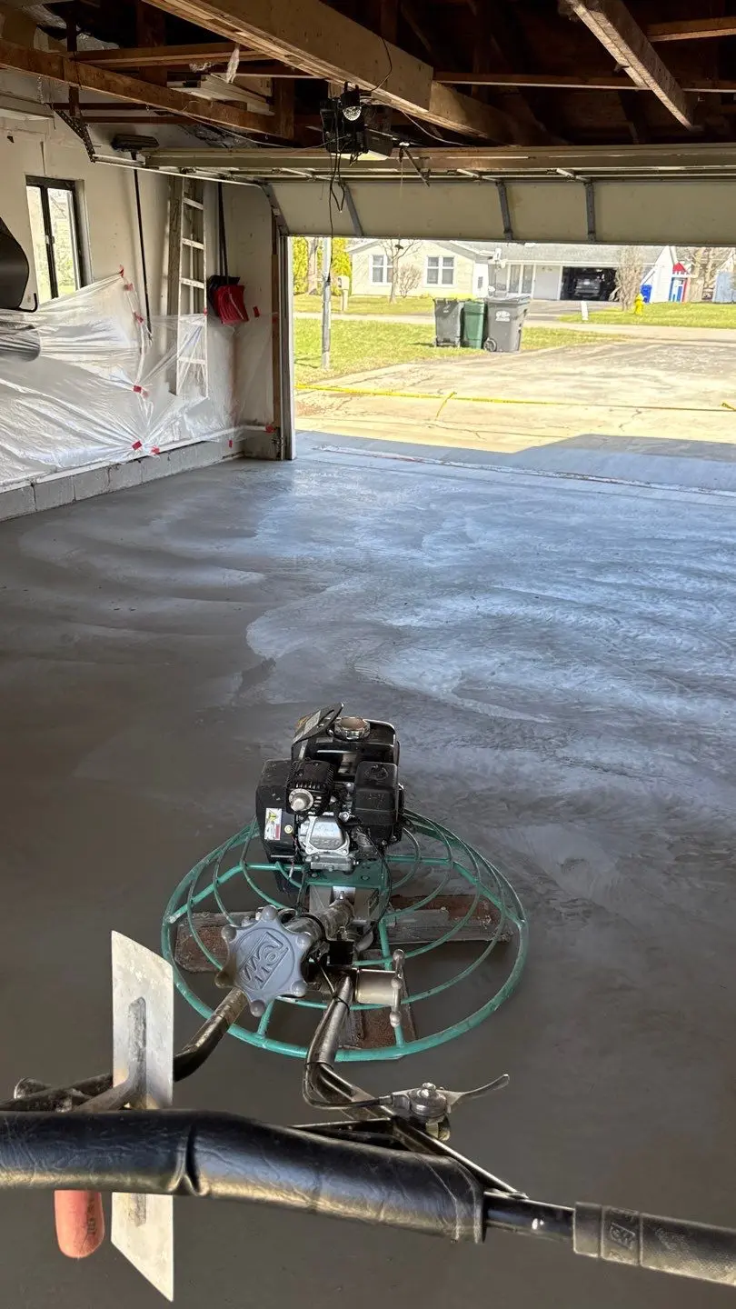 Power trowel working the fresh concrete garage floor in Greece NY with the walls masked in plastic sheeting