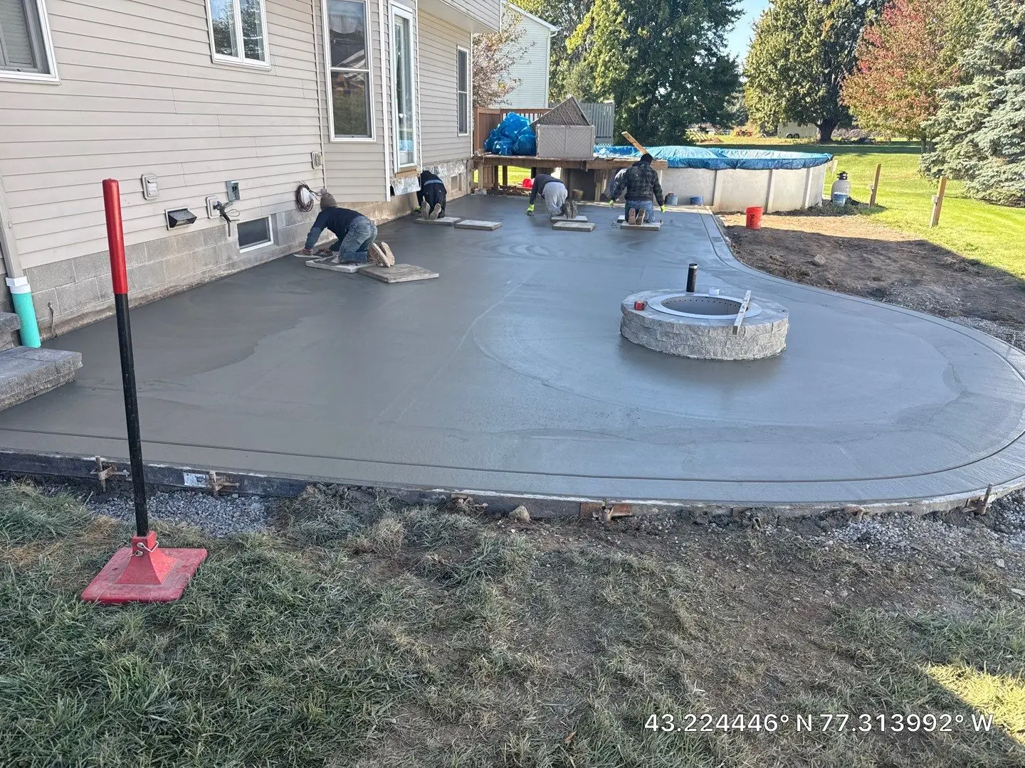 NG Masonry crew floating the fresh concrete patio slab in Ontario NY with the stone fire pit ring already set into the pour