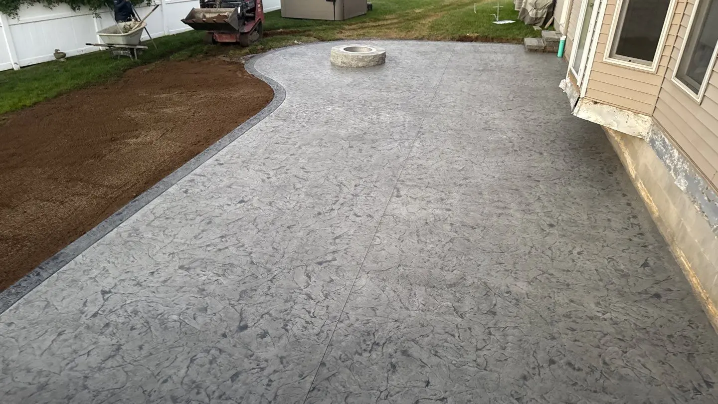 Seamless textured stamped concrete patio in Ontario NY with a contrasting smooth border and a round wood burning fire pit