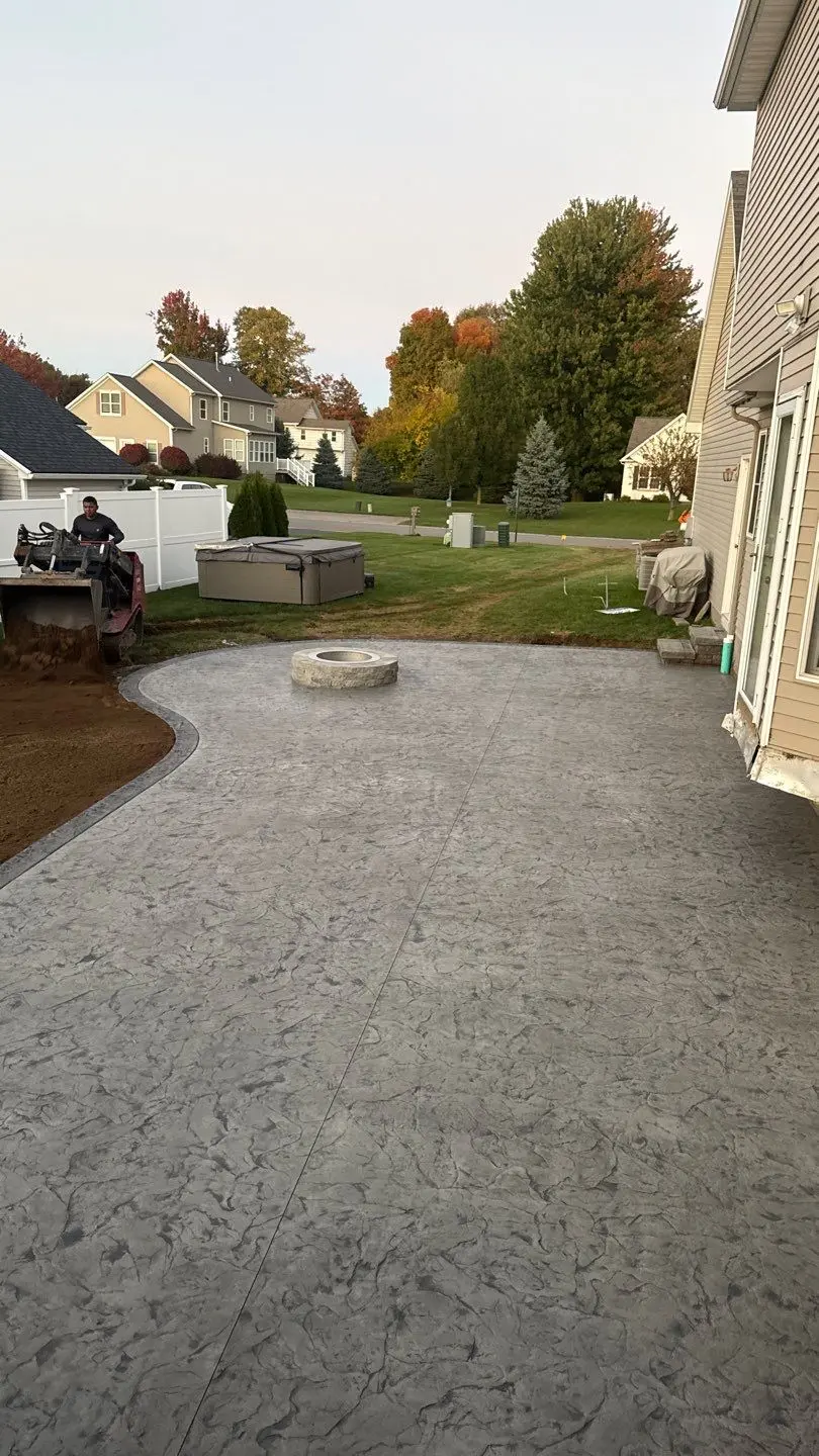 Finished stamped concrete patio in Ontario NY at dusk with the fire pit, the hot tub set back in place, and topsoil going down alongside