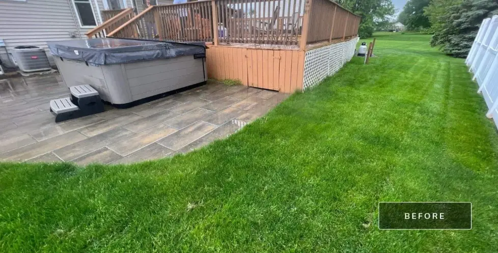 The back of the Ontario NY home before work started, with the aging wood deck, a hot tub sitting on the existing paver patio, and the lawn beyond