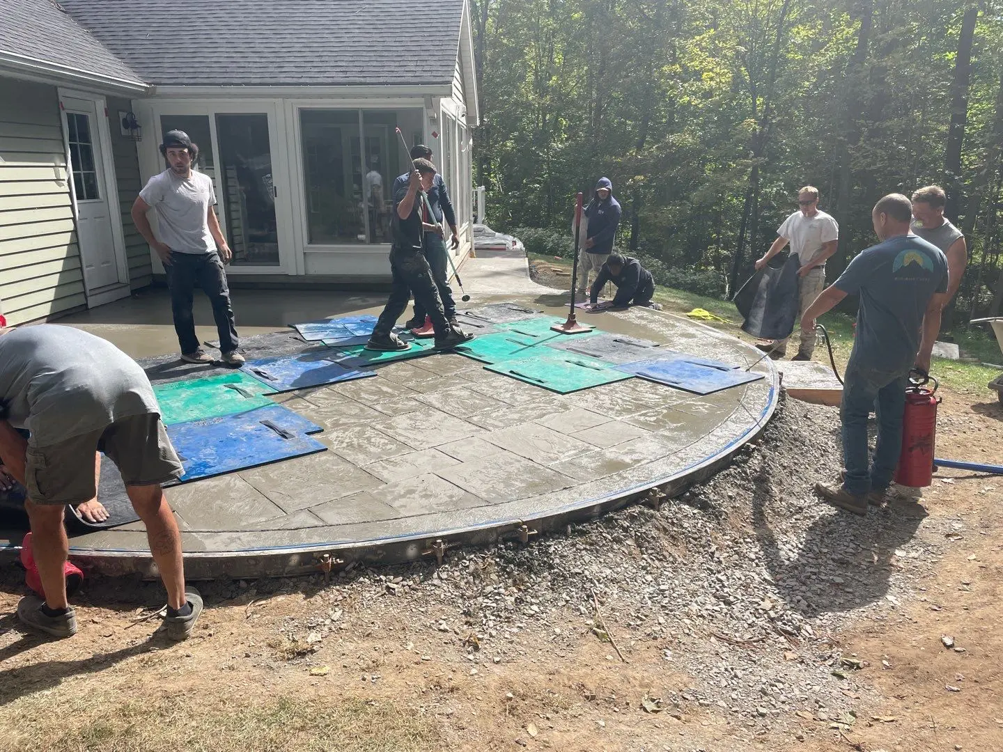 NG Masonry crew stamping the wet concrete patio in Pittsford NY with the curved form board staked around the edge