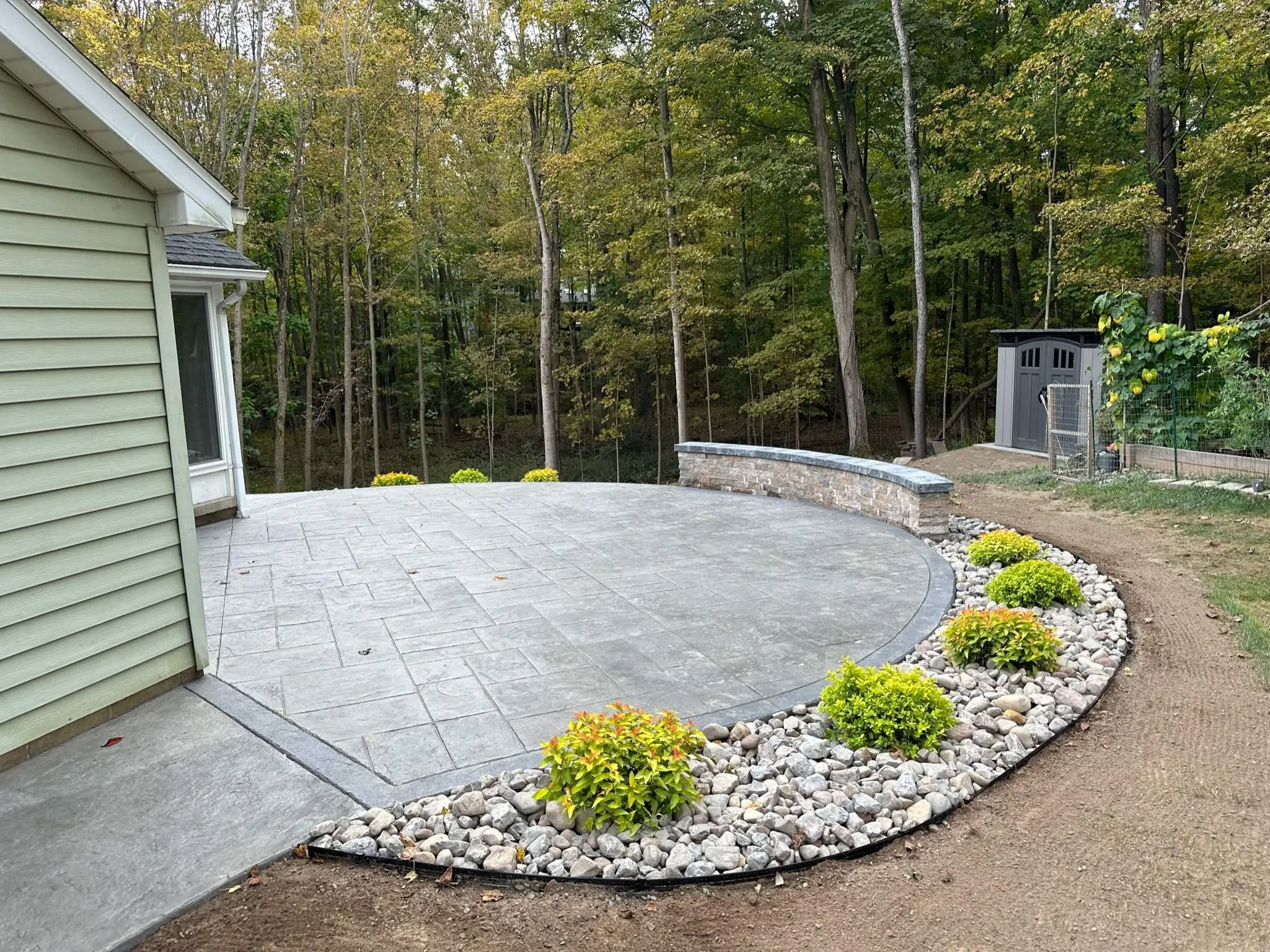 Curved Majestic Ashlar stamped concrete patio in Pittsford NY with a capped block wall and a river rock border