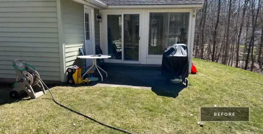The Pittsford NY backyard before work started, a small concrete slab off the sunroom door with the lawn sloping away toward the tree line